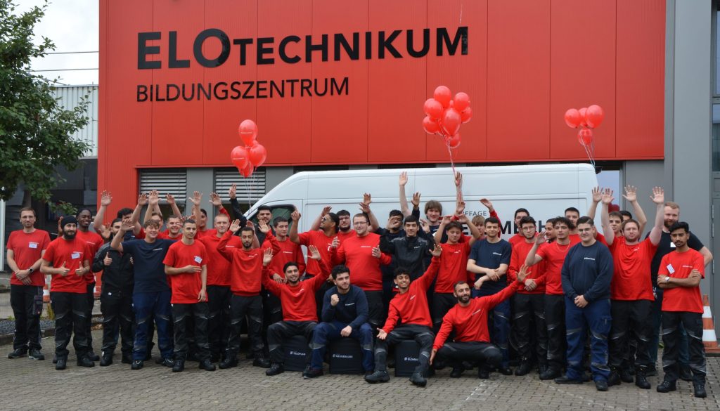 Gruppenbild aller Auszubildenden in Dienstkleidung vor dem ELOTechnikum Bildngszentrum der ELOMECH-GRUPPE am Hauptsitz in Mülheim an der Ruhr.